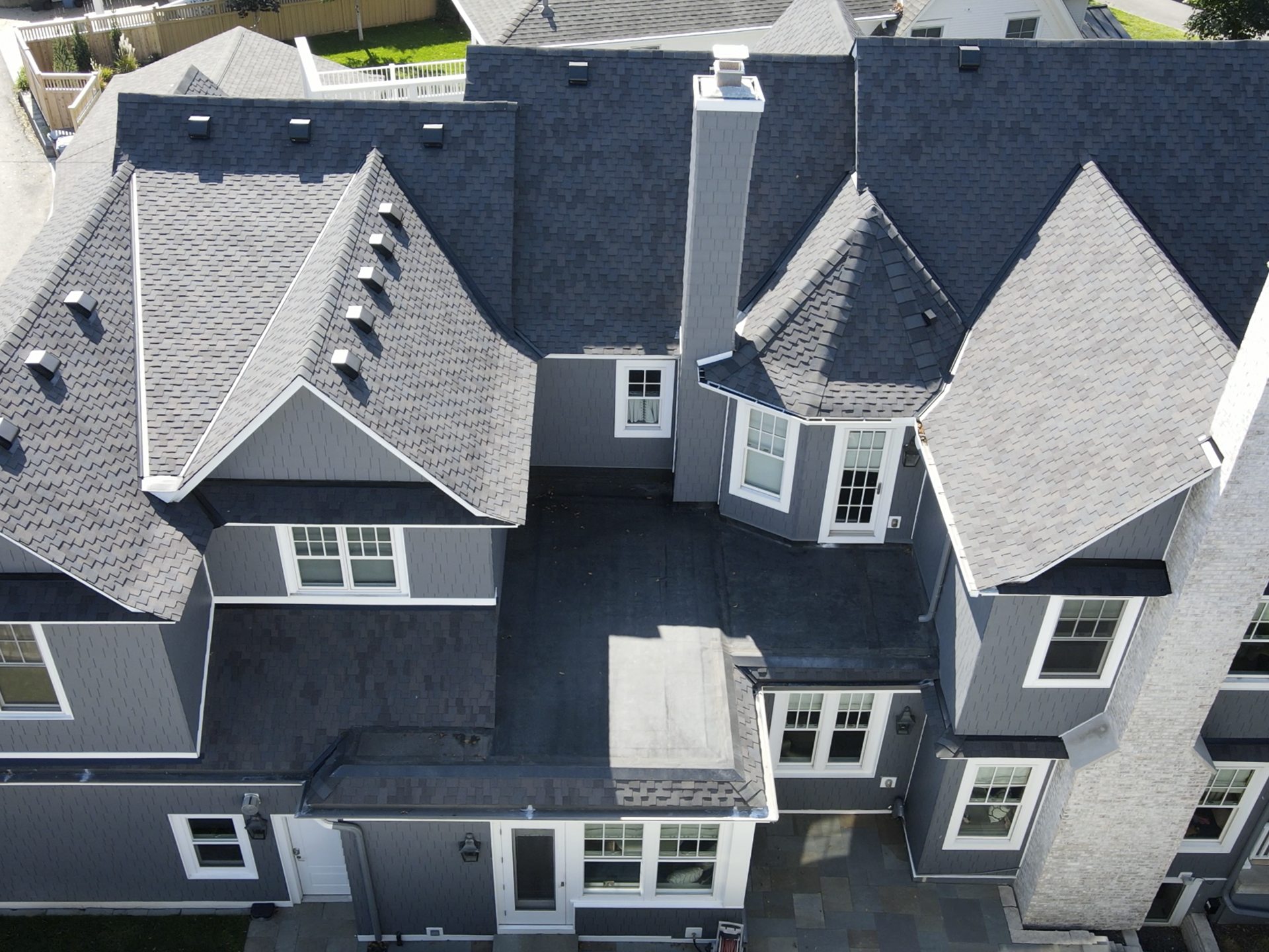 Complex Roof Structure Completed on Lake of the Isles Residence Top-down view of a large, two-story home with a complex roof structure featuring multiple gables, dormers, and steep pitches. The roof has dark shingles and precise detailing around chimneys and bay windows, showcasing Les Jones Roofing’s expert craftsmanship in Lake of the Isles.